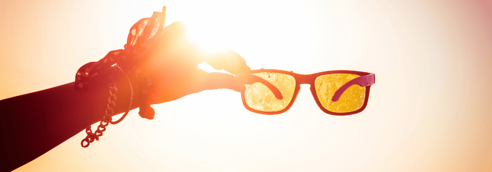 Die Hand hält die Sonnenbrille, die Sonne dahinter